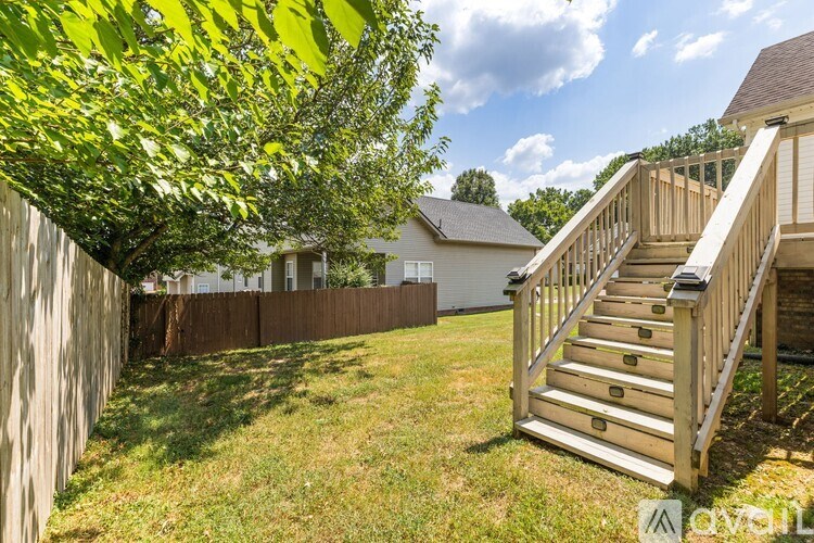 A wooden staircase leads up to a house with a white fence and a tree in the foreground.