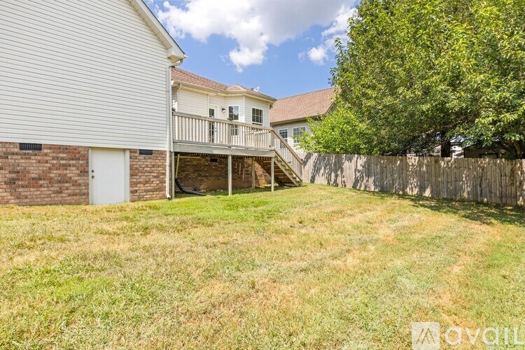 A backyard with a white house, a tree, and a wooden fence.