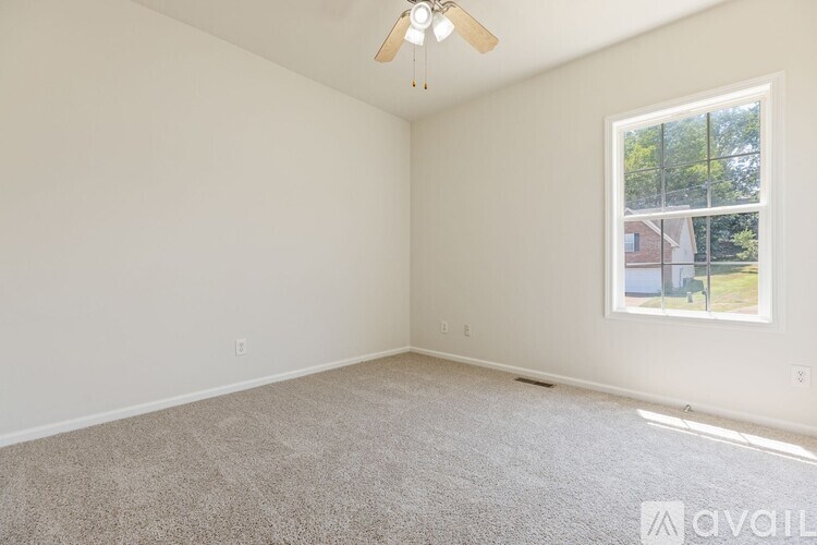 A room with a ceiling fan and a window showing a view of a house.