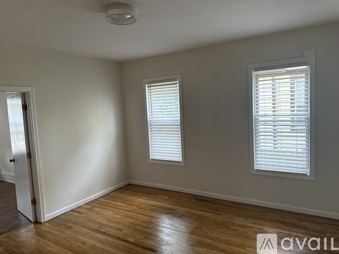 A room with wooden floors and two windows with blinds.