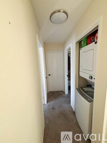 A narrow hallway with a white door and a white cabinet with a fridge on it.