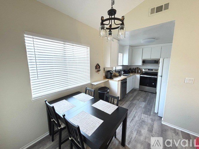 A dining room with a table set for four and a kitchen in the background.