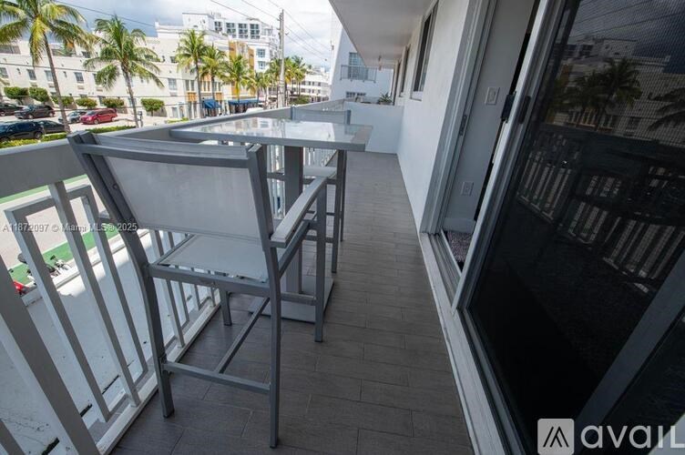 A balcony with a table and chairs overlooks a street with palm trees.