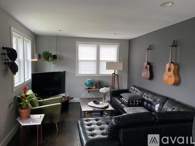 A living room with a black leather couch, a green armchair, a flat screen TV, and a guitar wall hanging.