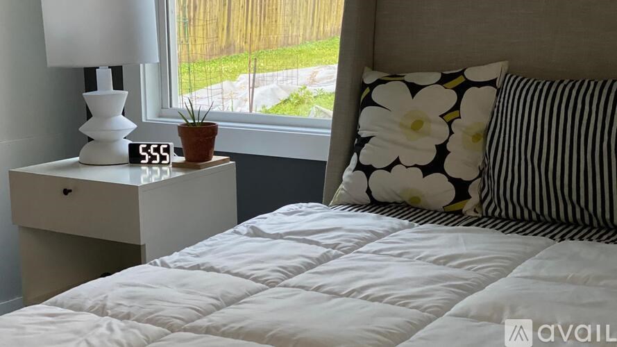A white bed with a white quilt and a white nightstand with a lamp on it.