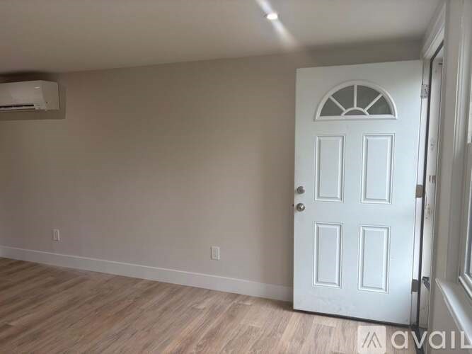 A white door with a window in the middle is in a room with wooden floors and an air conditioner on the wall.