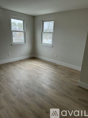A room with wooden flooring and two windows.