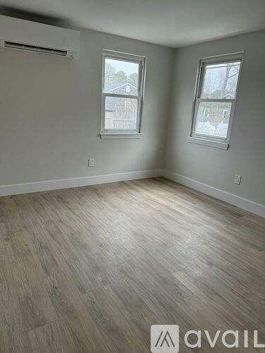 A room with wooden flooring and two windows.