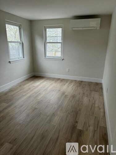 A room with wooden flooring and two windows.