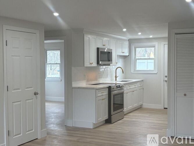 A kitchen with white cabinets and appliances, a window, and a door leading to another room.