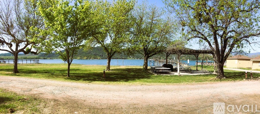 A tree-lined pathway leads to a pavilion by a lake.