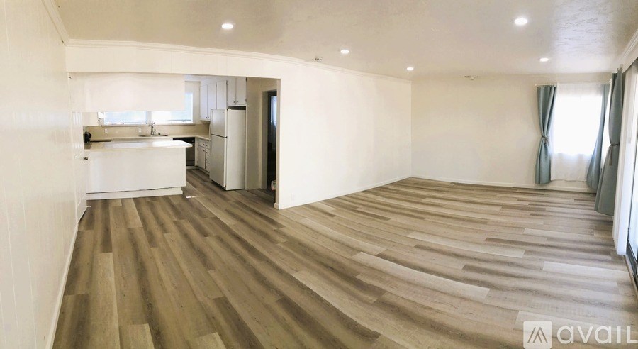 A spacious room with wooden flooring and a kitchen area in the background.