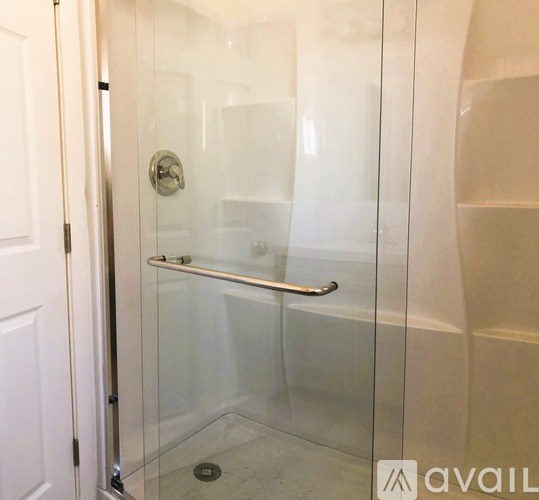 A glass shower door with a silver handle and a drain in the middle of the floor.