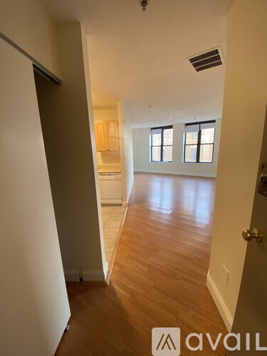 A hallway with wooden floors and white walls leading to a kitchen area.