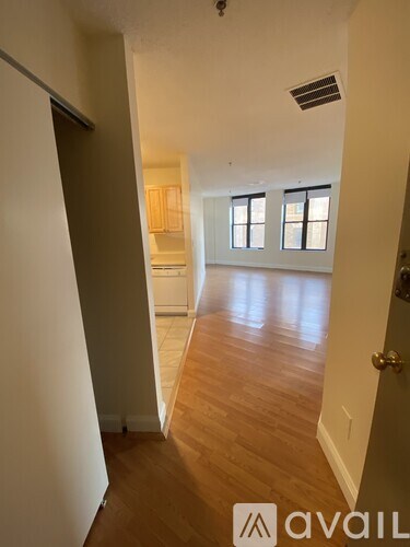 A hallway with wooden floors and white walls leading to a kitchen area.