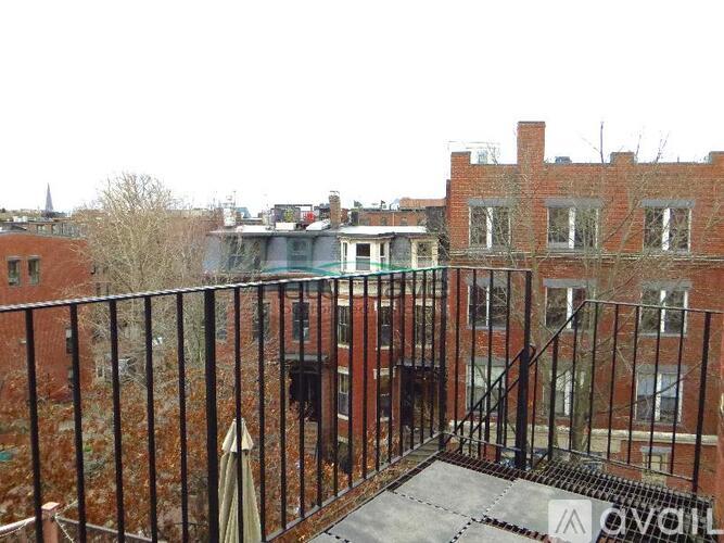 A balcony with a metal railing overlooks a courtyard with a building in the background.