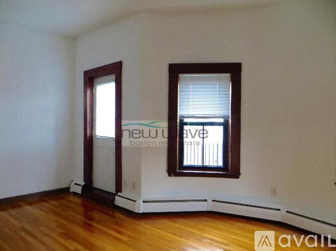 A room with wooden floors and two windows, one of which has blinds.
