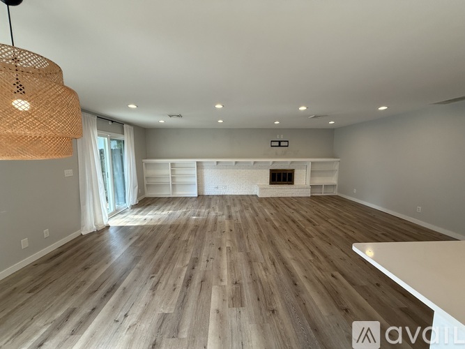 A spacious room with wooden flooring and a fireplace.