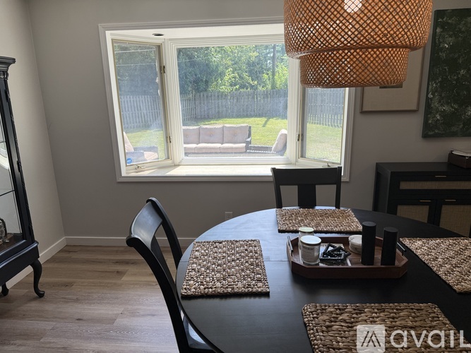 A dining room with a table set for two and a view of a backyard through the window.