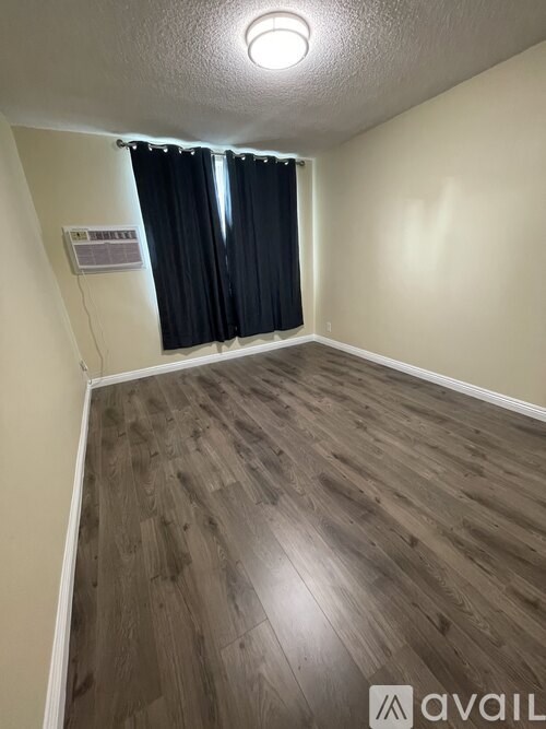 A room with wooden flooring and a window with black curtains.