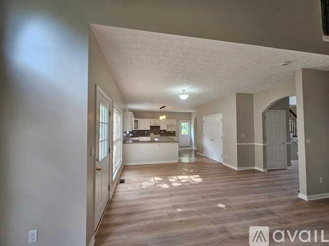 A spacious living room with hardwood floors and a kitchen in the background.