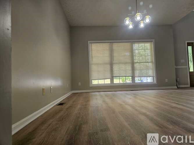 A spacious room with wooden floors and a large window with blinds.