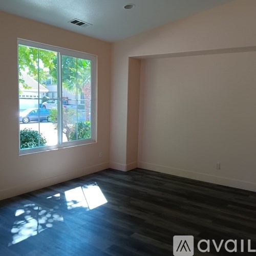 A room with a large window and a view of a street with cars and houses.