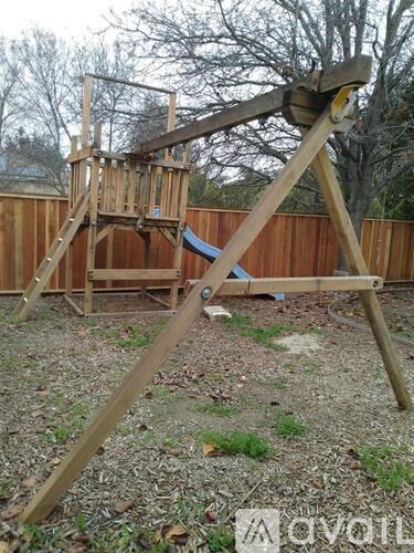 A wooden swing set with a blue slide in the backyard.
