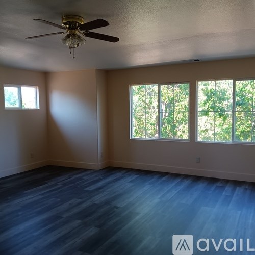 A room with a ceiling fan and large windows.