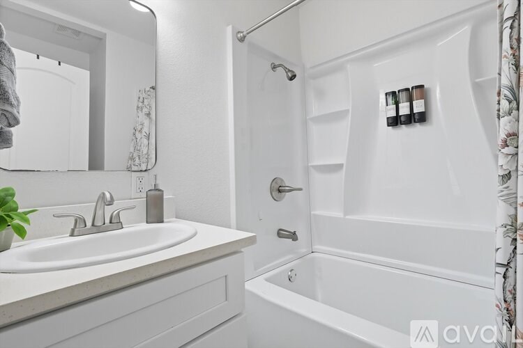 A white bathroom with a sink, mirror, and bathtub.