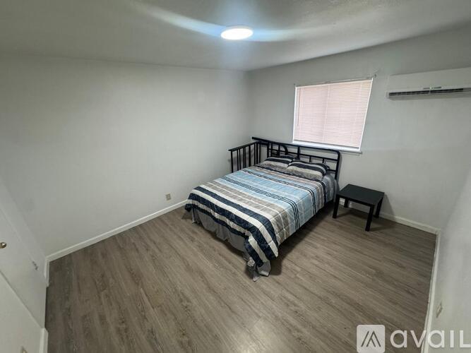 A bedroom with a bed, a small table, and a window with blinds.