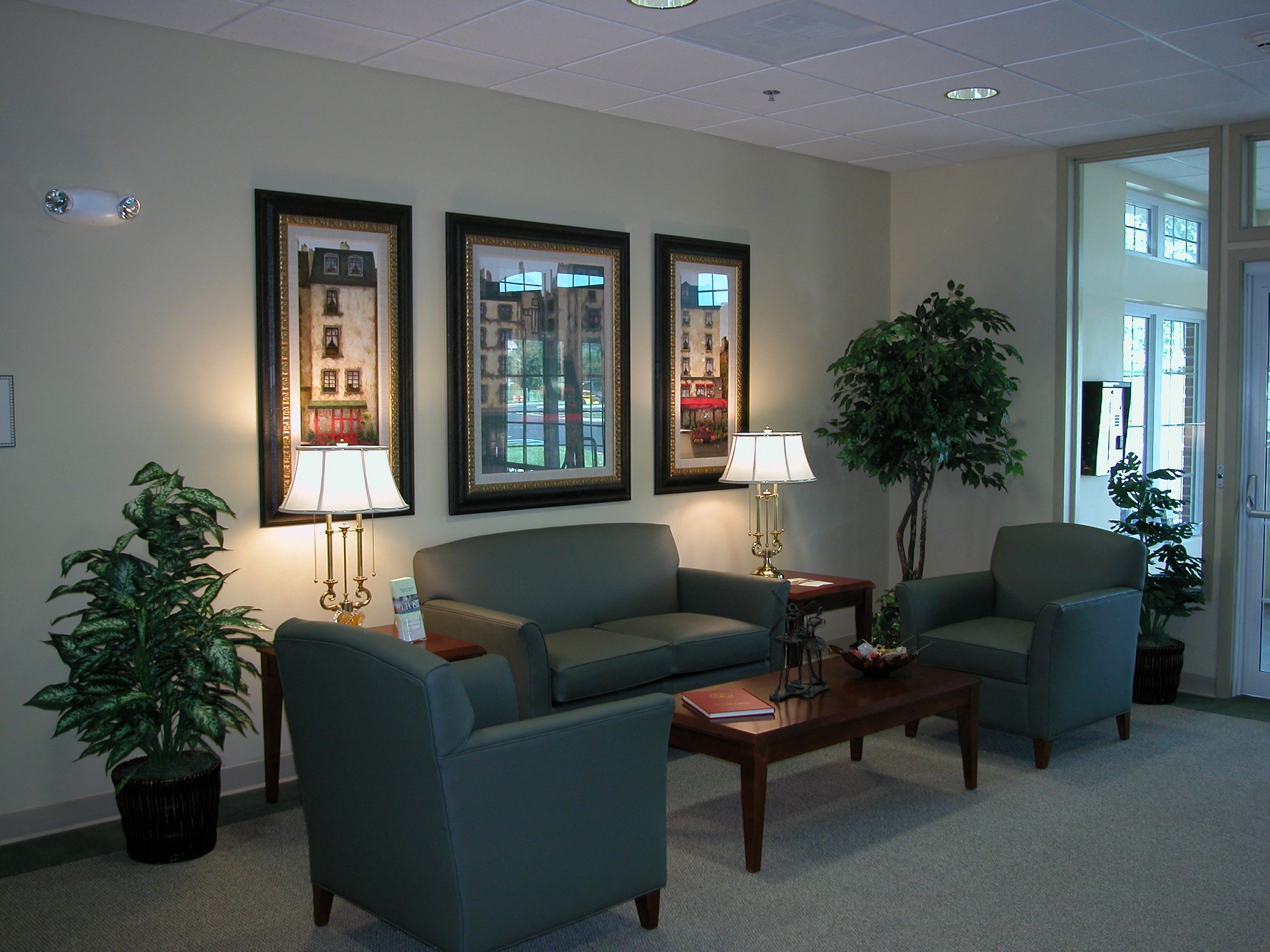 a waiting room with couches chairs and plants and three pictures on the wall