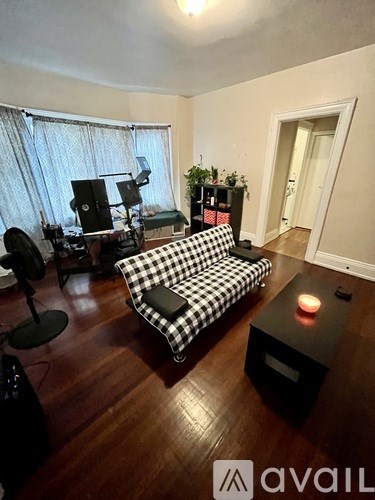 A black and white checkered sofa in a room with wooden floors and a window with curtains.