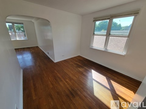 A room with wooden floors and white walls, with a window and a view of trees outside.