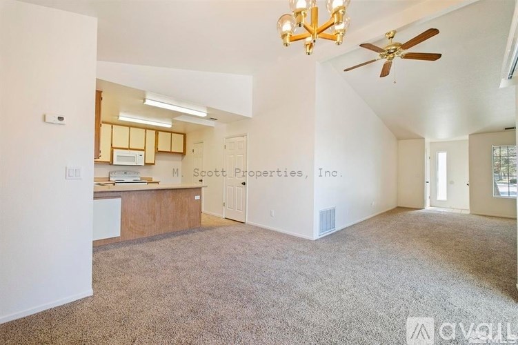 A spacious living room with a ceiling fan and a kitchen area in the background.