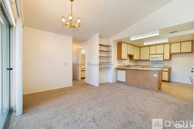 A spacious room with a chandelier and a kitchen area with wooden cabinets.