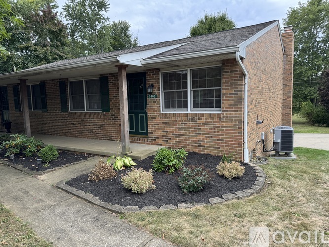 A small brick house with a green door and a landscaped front yard.