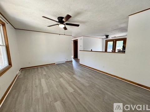 A room with a ceiling fan and light, wooden flooring, and a window with blinds.