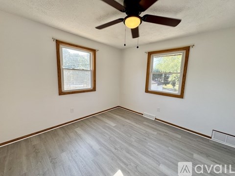 A room with a ceiling fan and two windows.