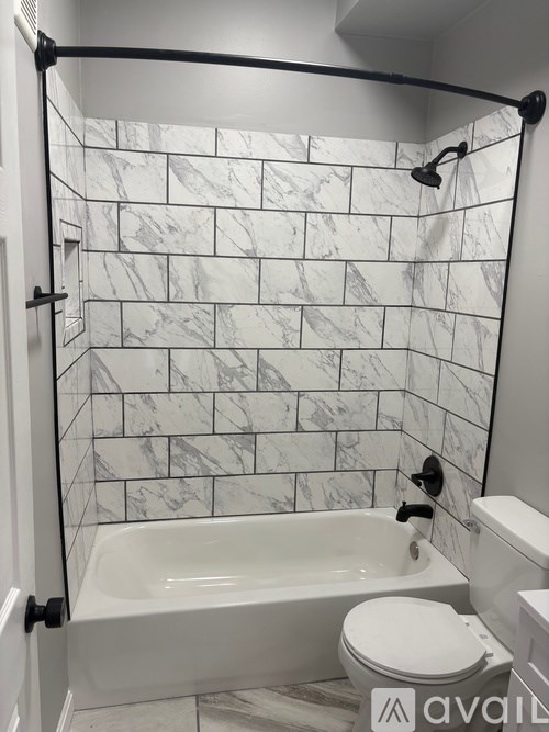 A bathroom with a marble tile shower and white fixtures.