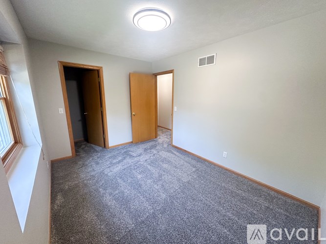A carpeted room with two doors and a window.