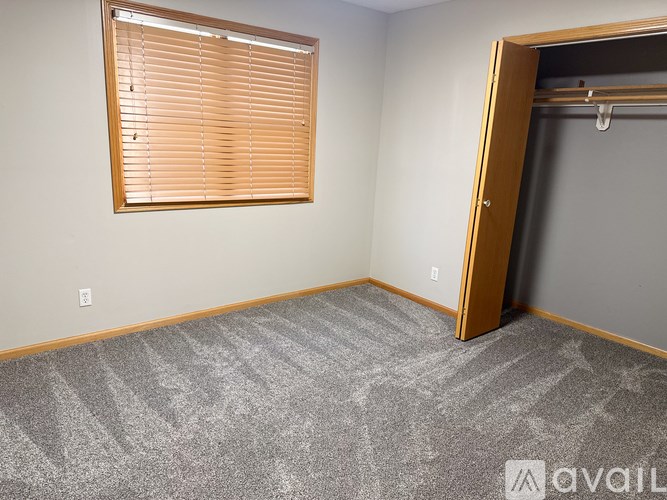 A room with a carpeted floor, a window with blinds, and a door.