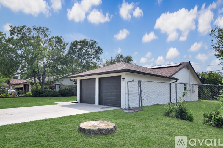 A two-car garage with a brown roof is surrounded by a fence and greenery.