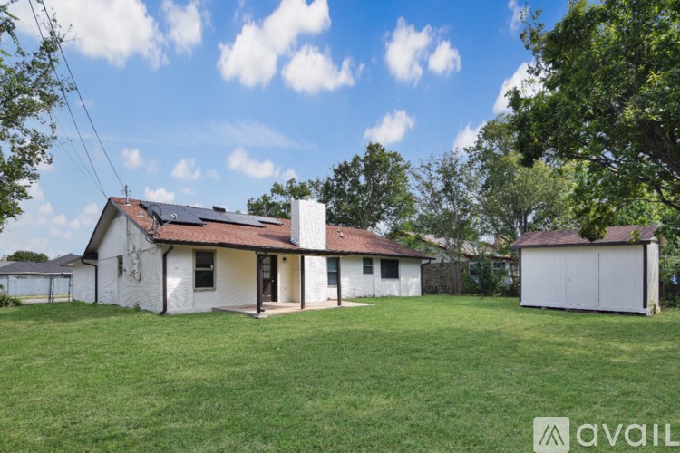 A house with a white exterior and a red roof is surrounded by a grassy lawn.