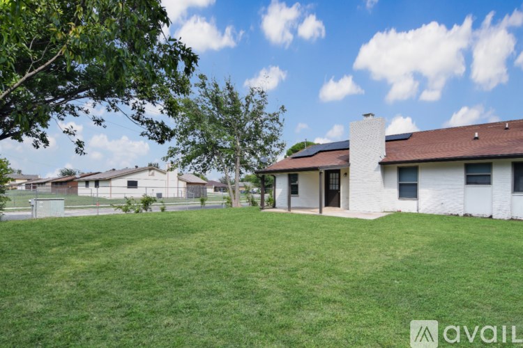 A white house with a brown roof and a chimney is surrounded by a green lawn.