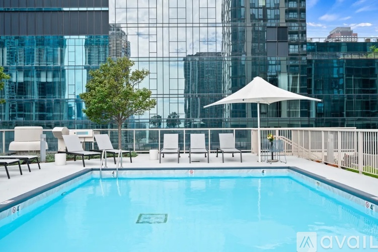 A pool with chairs and an umbrella on a balcony with buildings in the background.