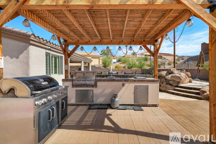 A wooden pergola over an outdoor kitchen with a grill and sink.