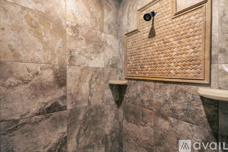 A shower with a brown tile wall and a gold tile shower head.