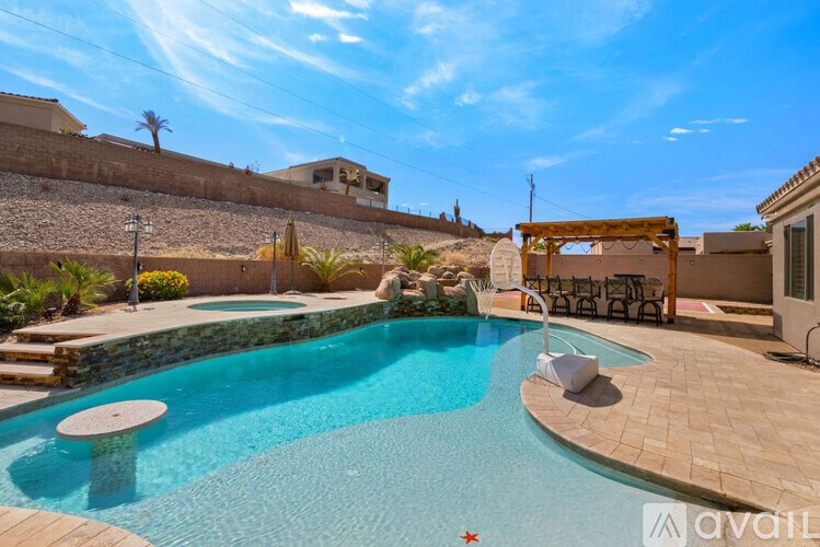 A pool with a stone wall and a wooden pergola.