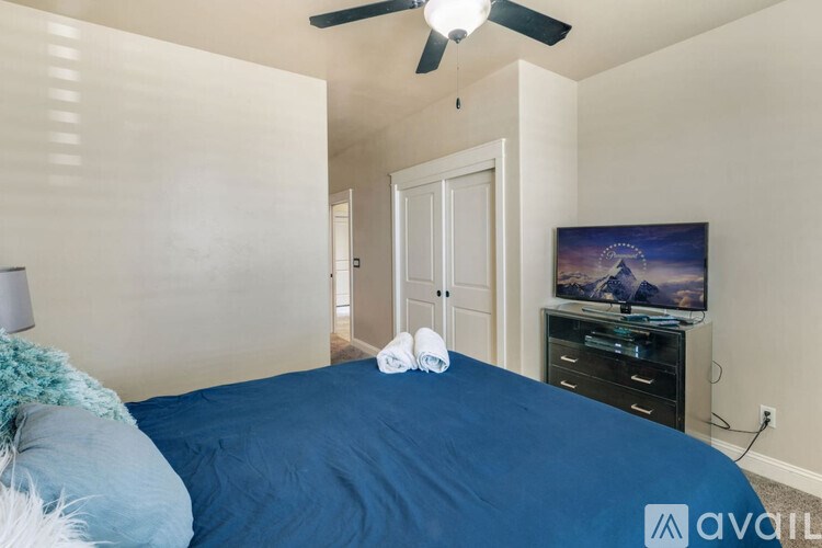 A bedroom with a blue bedspread and a ceiling fan.